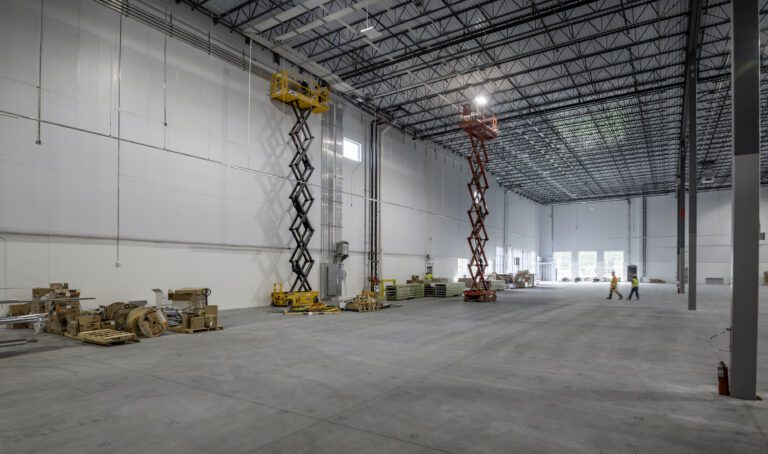 Scissor lifts along the perimeter wall as crews run aluminum EMT conduit at Amazon SNJ5, Jersey City NJ